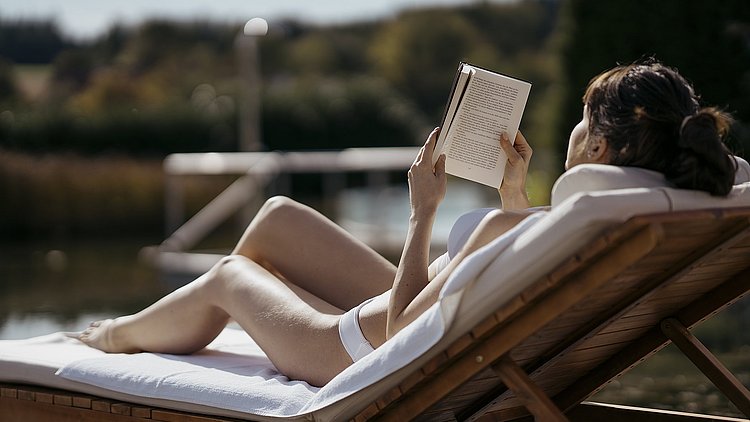Eine Frau liegt im Spa Resort Therme Geinberg im Innviertel auf einer Liege und liest entspannt ein Buch.