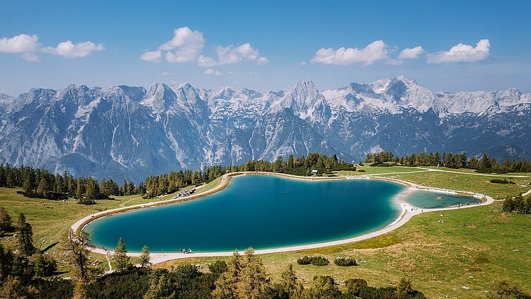 Der Schafkogelsee auf der Höss in Hinterstoder aus der Vogelperspektive. Ebenso zu sehen ist das Panorama des Toten Gebirges, mit der Spitzmauer, dem Brotfall, dem Großen Priel und weiteren Gipfeln.