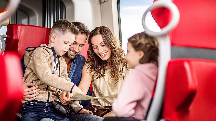 Mobil ans Ziel: Eine Familie sitzt im Zug und freut sich auf den Ausflugstag.