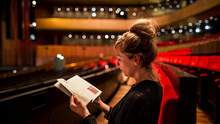 Eine Frau sitzt im Musiktheater Linz und betrachtet ein Prospekt