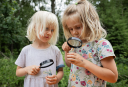 Zwei Mädchen betrachten durch eine Lupe Insekten.
