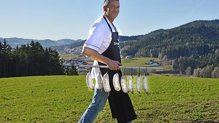 Der Chef der Salamitrochnerei spaziert mit seinen Salami-Würsten durch die Wiese.