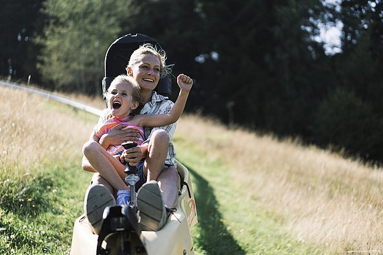 Foto Oberösterreich Tourismus/Traunsee-Almtal/Robert Maybach: Frau mit Mädchen auf der Sommerrodelbahn Grünberg-Flitzer im Salzkammergut.