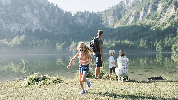 Eine Familie am Laudachsee in Grünberg im Salzkammergut. Mann, Frau und Bub stehen direkt am See and schauen in die Ferne. Das Mädchen läuft aufgeregt in Richtung Kamera.