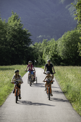 Eine Familie fährt auf einem Radweg zwischen Wiesen und Bäumen.