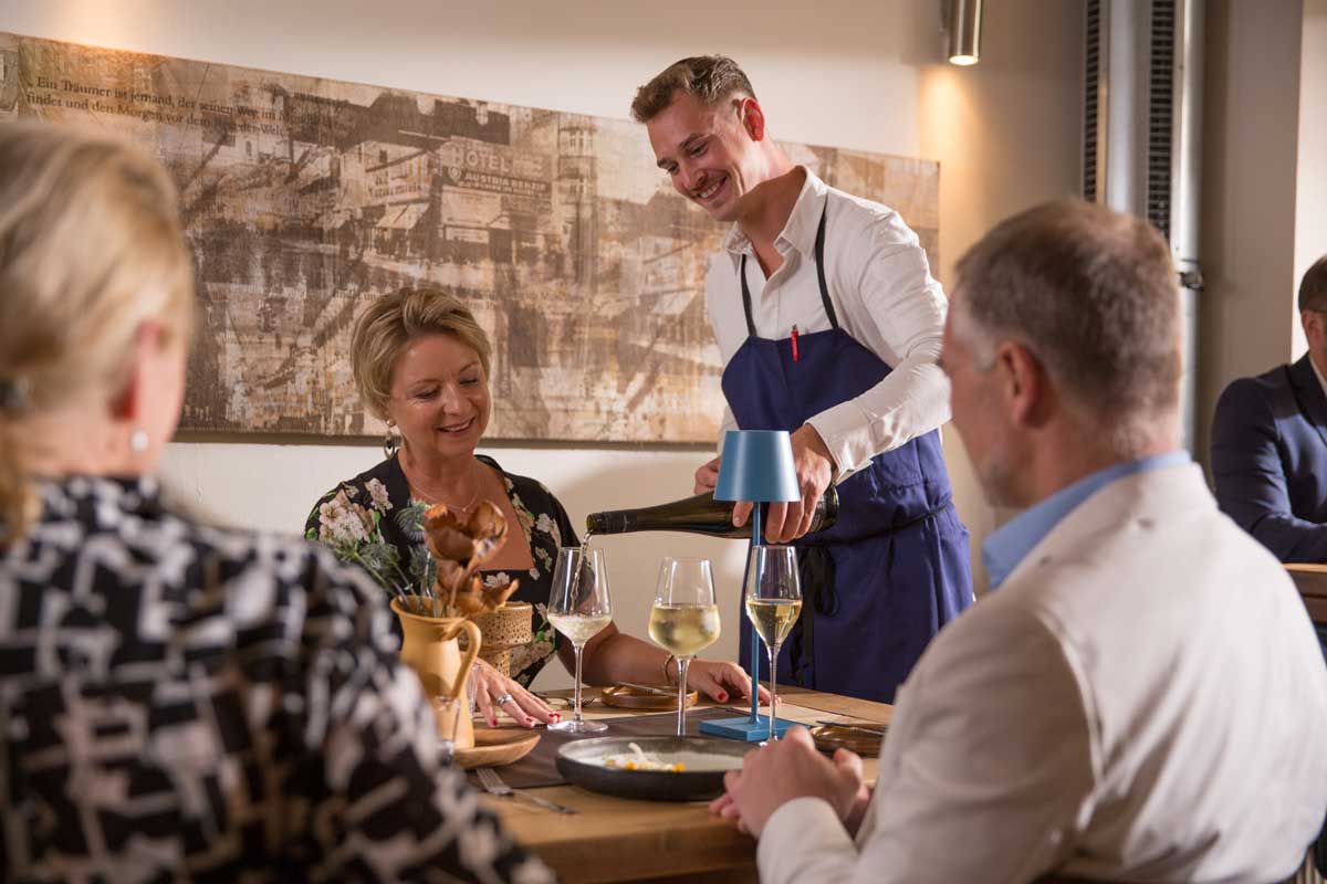 Ein Servicemitarbeiter schenkt den Gästen der Huberei Wein ein.