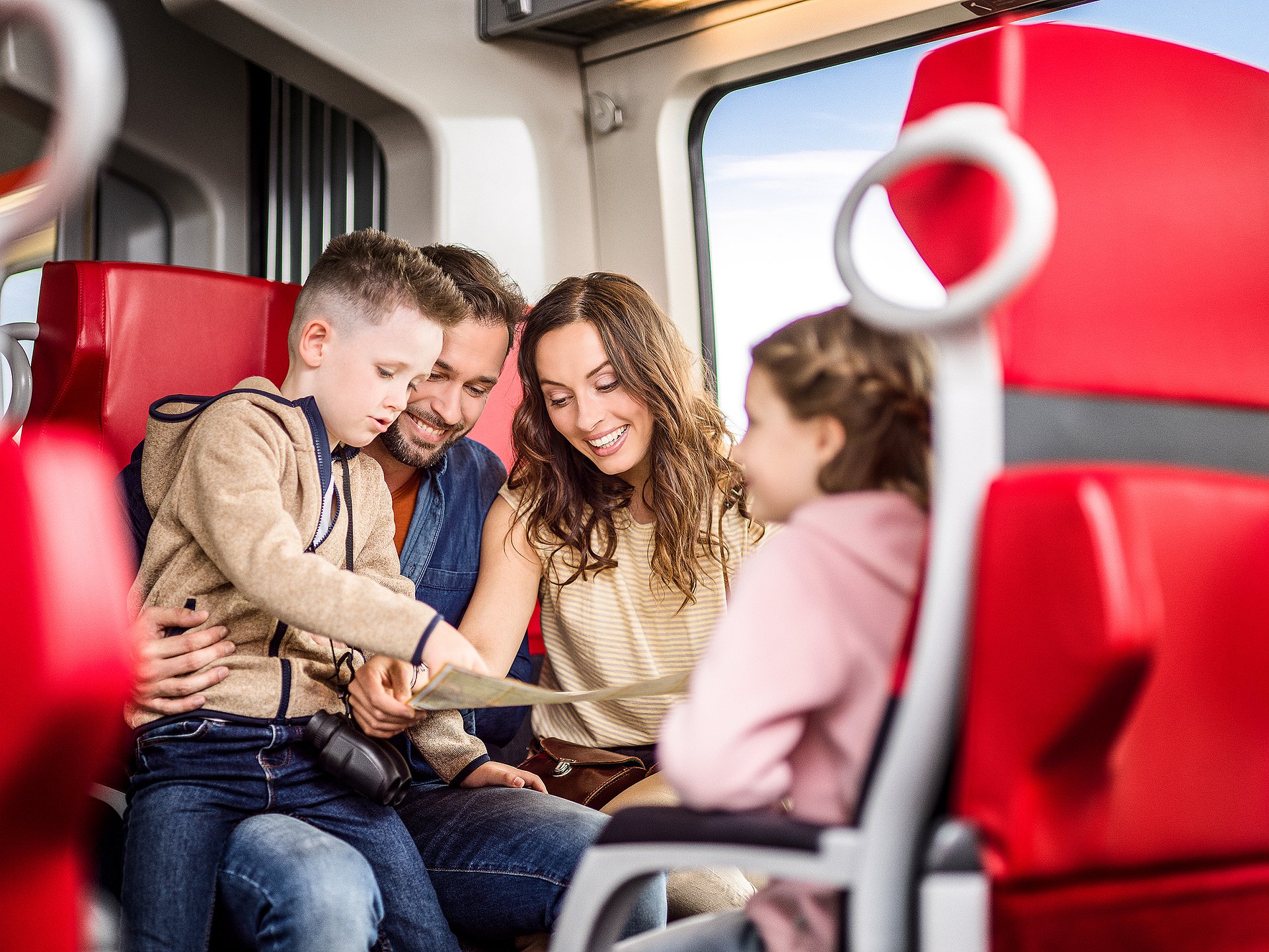 Mobil ans Ziel: Eine Familie sitzt im Zug und freut sich auf den Ausflugstag.
